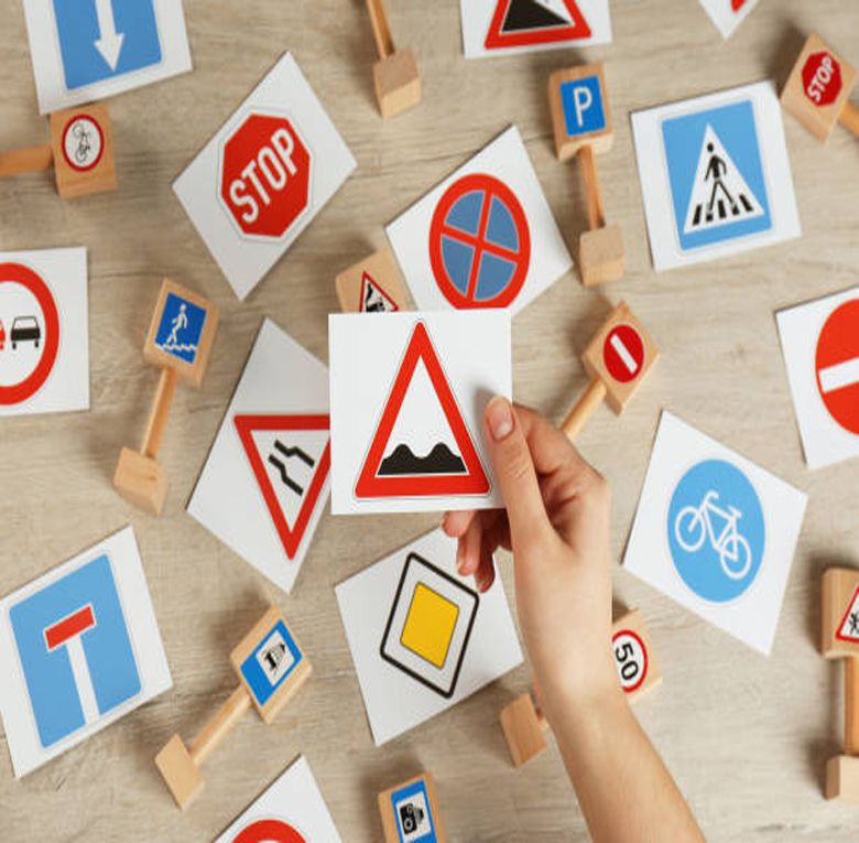 Woman holding rough road sign over wooden table, top view. Driving license exam